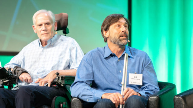 Erik speaking on stage with Claude on his right and Aimee on his left.